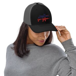 Puede incluir: Una gorra de camionero negra y gris con un gráfico rojo, blanco y azul de un rifle y el texto "The 2A Crew".