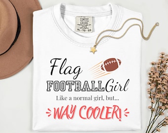 May include: White t-shirt with the text "Flag FOOTBALL Girl" and a football graphic. The shirt also has the text "Like a normal girl, but... WAY COOLER!". A gold necklace with a star pendant is on the shirt.
