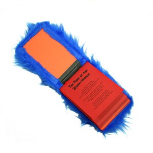 May include: A red book with the title "The Name of the Woman/Weasel" is open and partially visible. The book is covered in blue faux fur.