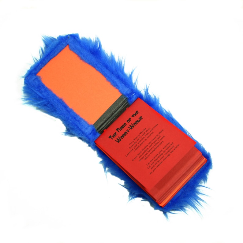 May include: A red book with the title "The Name of the Woman/Weasel" is open and partially visible. The book is covered in blue faux fur.