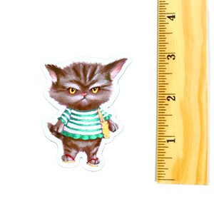 May include: A grumpy-looking cat wearing a green and white striped shirt and carrying a yellow bag. The cat is brown and has yellow eyes.