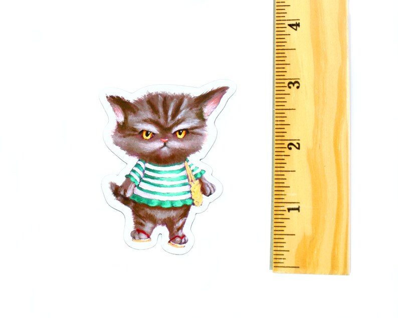 May include: A grumpy-looking cat wearing a green and white striped shirt and carrying a yellow bag. The cat is brown and has yellow eyes.