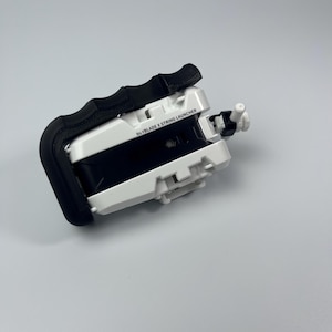 Puede incluir: Lanzador de cuerda Beyblade X blanco y negro con un asa negra. El texto "Beyblade X String Launcher" est&aacute; impreso en el lateral. El lanzador tiene una peque&ntilde;a boquilla blanca y negra en el extremo.
