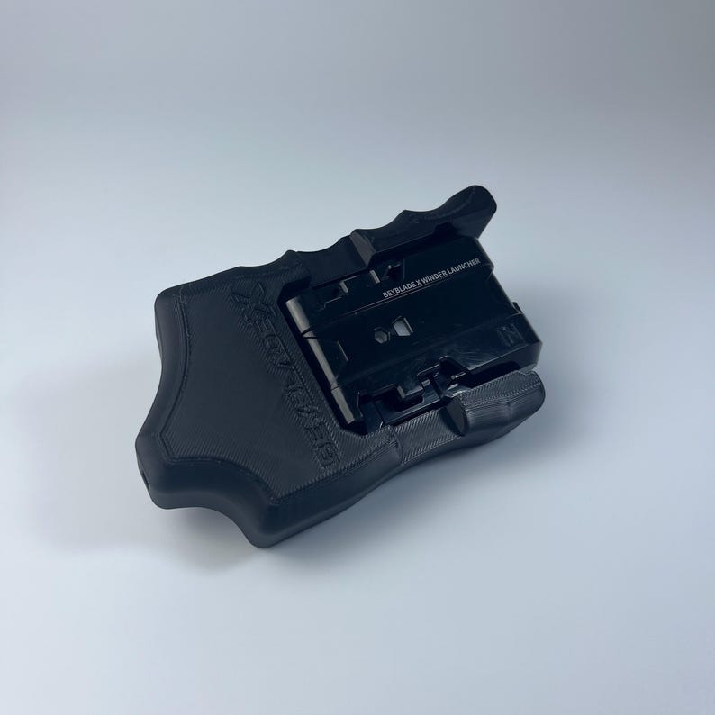 Puede incluir: Un lanzador de peonzas Beyblade X negro. El lanzador es negro con el texto "BEYBLADE X WINDER LAUNCHER" impreso en la parte superior. El lanzador est&aacute; dise&ntilde;ado para sujetarse con la mano y tiene un mecanismo de gatillo.