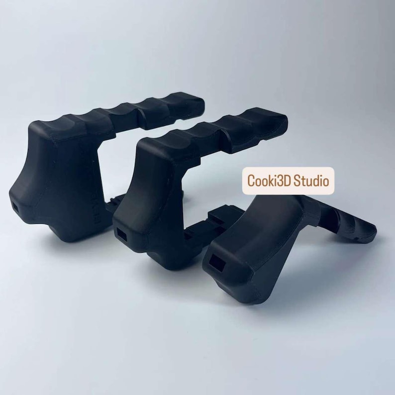Puede incluir: Tres empu&ntilde;aduras negras para c&aacute;mara con agarre texturizado. Las empu&ntilde;aduras son de material mate y tienen un dise&ntilde;o curvo. El texto "Cooki3D Studio" es visible en la imagen.