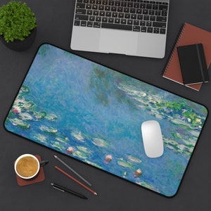 May include: A rectangular desk mat featuring a water lilies painting in shades of blue, green, and pink. The mat has a black border and a white computer mouse is on the mat. A laptop, notebooks, and a cup of coffee are also visible.