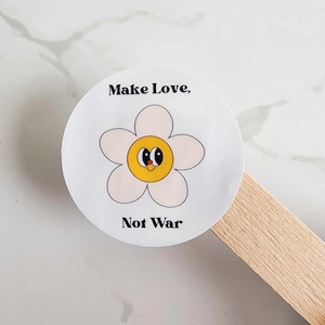 Könnte beinhalten: Runder weißer Aufkleber mit einer gelben Blume mit einem Smiley-Gesicht und dem Text "Make Love, Not War."