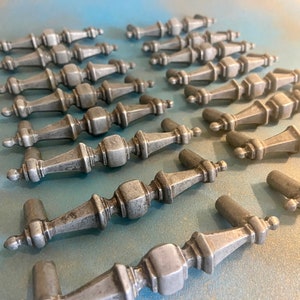 May include: A collection of 18 silver-toned cabinet knobs with a decorative, ornate design. The knobs have a vintage, antique look and are arranged in rows on a blue surface.