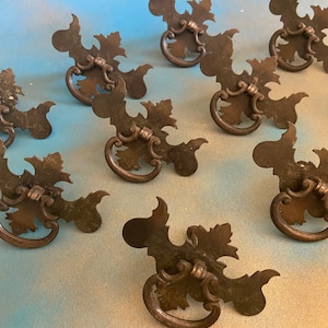 May include: Eight antique bronze cabinet door pulls with a leaf design. The pulls have a ring handle and are in good condition.
