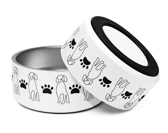 Puede incluir: Dos cuencos blancos para perros con interior de acero inoxidable. El exterior presenta un patrón repetido de perros y huellas de patas negras dibujados con líneas. Un cuenco está ligeramente inclinado, revelando la base de goma negra.