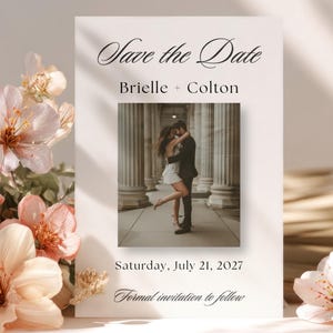 May include: A white wedding invitation with the text "Save the Date" and the names "Brielle + Colton". It includes a photo of a couple embracing. The date "Saturday, July 21, 2027" is also displayed. Floral arrangement in the background.