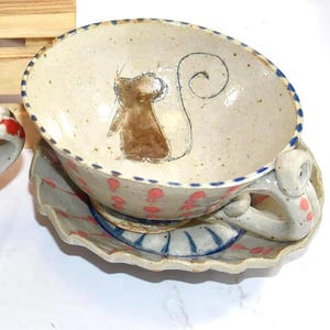 Puede incluir: Juego de taza y platillo de t&eacute; de cer&aacute;mica pintados a mano. La taza presenta una ilustraci&oacute;n de rat&oacute;n marr&oacute;n y un borde punteado azul. El platillo tiene un borde festoneado y lunares rosas. El asa tiene una forma &uacute;nica.