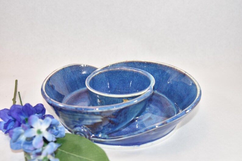 May include: A blue ceramic serving dish with a smaller bowl in the center. The dish has a unique shape and a speckled glaze.