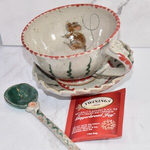 Puede incluir: Un juego de taza y platillo de cer&aacute;mica con un dise&ntilde;o de rat&oacute;n pintado a mano. El juego incluye una cuchara a juego y un paquete de t&eacute; Twinings Gingerbread Joy. La taza y el platillo tienen detalles en rojo y verde.