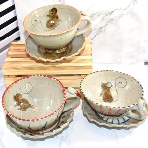 Puede incluir: Tazas de t&eacute; y platillos de cer&aacute;mica hechos a mano con ilustraciones de ratones. Las tazas tienen un color base beige con un dise&ntilde;o de rat&oacute;n y un platillo a juego. Los bordes est&aacute;n decorados con detalles en rojo, rosa y azul.