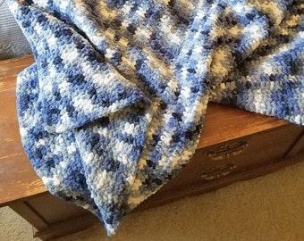 Könnte beinhalten: Eine blaue und weiße gehäkelte Decke mit einer strukturierten, flauschigen Optik. Die Decke ist gefaltet und über eine Holzkiste gelegt.