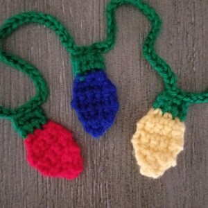 May include: A string of crocheted light bulbs in red, blue, and yellow. The bulbs are connected by green crocheted strings.