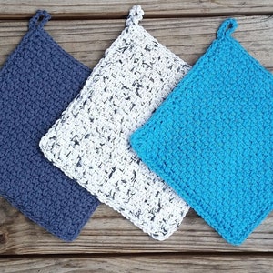 May include: Three crocheted pot holders in different colors: blue, white with black flecks, and turquoise. The pot holders are square shaped with a loop at the top.