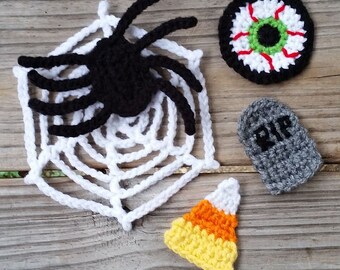 May include: A set of five crocheted Halloween decorations, including a spider on a web, a candy corn, a tombstone with the inscription "RIP", and a large eyeball.