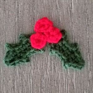 May include: A green crocheted holly leaf with three red crocheted berries.