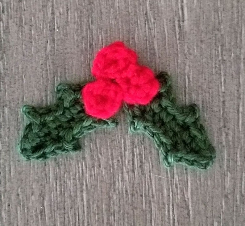 May include: A green crocheted holly leaf with three red crocheted berries.