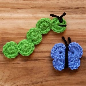 May include: A green crocheted caterpillar with a black face and a blue crocheted butterfly with black antennae.