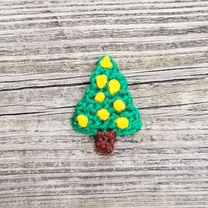 May include: A green crocheted Christmas tree ornament with yellow felt baubles and a brown felt trunk.