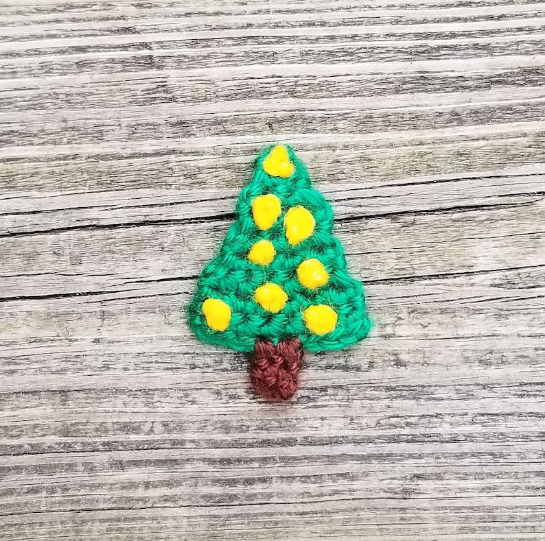 May include: A green crocheted Christmas tree ornament with yellow felt baubles and a brown felt trunk.