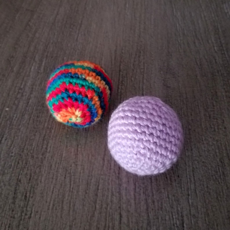 May include: Two crocheted balls, one with a rainbow pattern and the other a solid purple.