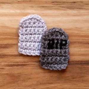 Puede incluir: Dos títeres de dedo de crochet, uno gris y otro blanco. El títere gris tiene las letras "RIP" bordadas.