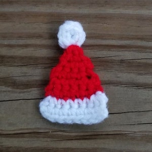 May include: A small red and white crocheted Santa hat with a white pom-pom on top.