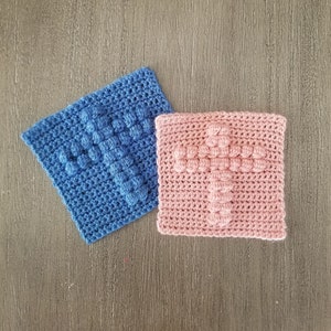 Puede incluir: Dos cuadrados de ganchillo con un diseño de cruz. Un cuadrado es azul y el otro es rosa.
