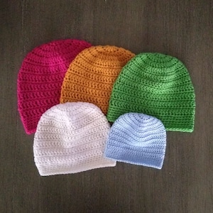 May include: Five crocheted hats in different colors and sizes. The hats are arranged in a pyramid shape, with the largest hat at the bottom and the smallest hat at the top. The hats are made of a soft, textured yarn. The colors of the hats are red, orange, green, white, and blue.
