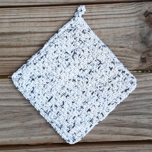 May include: A white and gray crocheted pot holder with a diamond shape.