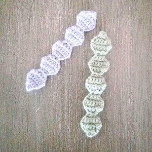 May include: Two crocheted chains, one in light purple and one in light green, are laid out on a wooden surface.