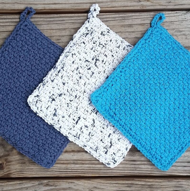 May include: Three crocheted pot holders in different colors: blue, white with black flecks, and turquoise. The pot holders are square shaped with a loop at the top.
