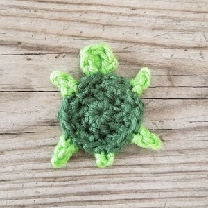 K&ouml;nnte beinhalten: Eine gr&uuml;ne geh&auml;kelte Schildkr&ouml;te mit einer hellgr&uuml;nen Schale und Beinen. Die Schildkr&ouml;te sitzt auf einer Holzoberfl&auml;che.
