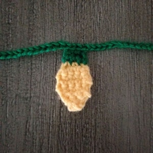 May include: A crocheted light bulb ornament with a green top and yellow body.