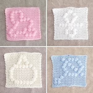 Op de afbeelding: Vier gehaakte vierkanten met een hartvormig ontwerp in verschillende kleuren: roze, wit, crème en lichtblauw.