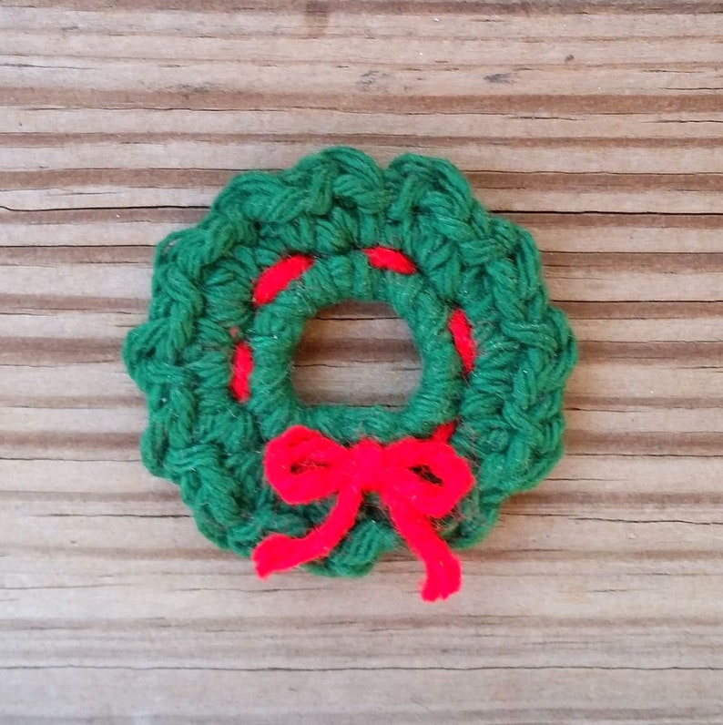 May include: A green crocheted wreath with a red bow. The wreath is made of yarn and has a simple design.