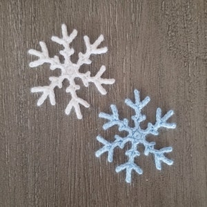 May include: Two crocheted snowflakes, one white and one light blue, rest on a textured, gray surface. The snowflakes have intricate, six-pointed designs, perfect for winter-themed crafts or decorations. The handmade quality is evident in the detailed stitching.