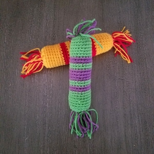 May include: A crocheted toy with a long, green and purple body and a shorter, yellow, red, and orange body. The toy has a long, fringed tail.