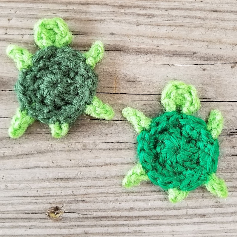 K&ouml;nnte beinhalten: Zwei geh&auml;kelte gr&uuml;ne Schildkr&ouml;ten mit hellgr&uuml;nen Akzenten. Die Schildkr&ouml;ten sind mit einem strukturierten Stich gearbeitet und haben eine runde Form.