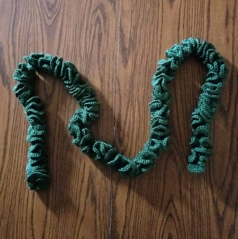 Pu&ograve; includere: Una sciarpa di uncinetto verde con un design a balze.