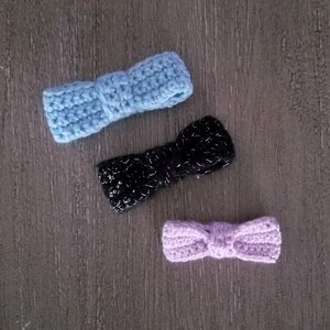 May include: Three crocheted hair bows in different colors: light blue, black with silver glitter, and light purple.
