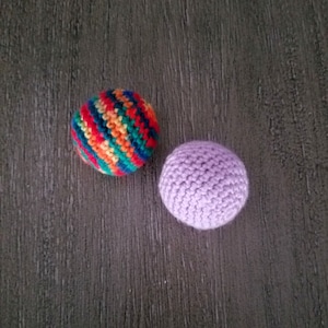 May include: Two crocheted balls, one with a rainbow striped pattern and the other a solid purple.