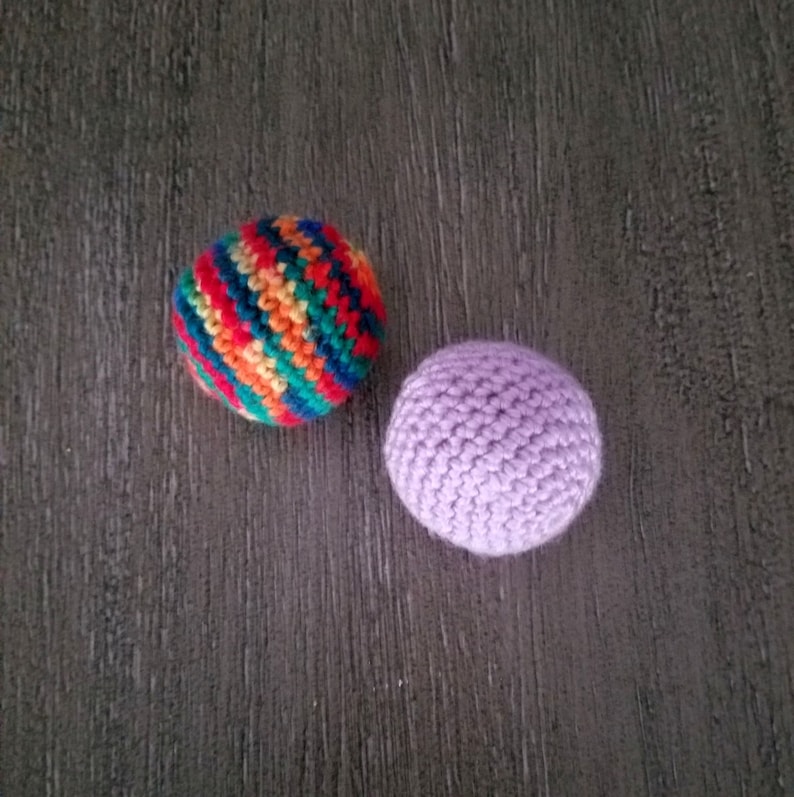 May include: Two crocheted balls, one with a rainbow striped pattern and the other a solid purple.