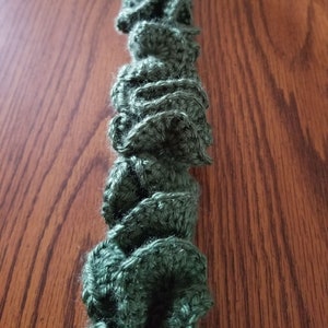 Pu&ograve; includere: Primo piano di una ghirlanda di uncinetto verde con una texture arricciata. La ghirlanda &egrave; fatta di filato e ha un aspetto morbido e peloso.