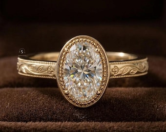 Peut inclure: Une bague en or avec une pierre précieuse transparente de taille ovale au centre, entourée d'une bordure perlée. L'anneau en or présente un motif de feuilles gravé sur les côtés, avec un petit logo visible sur le côté gauche de l'anneau.
