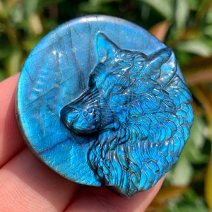 May include: A blue labradorite gemstone carved into the shape of a wolf's head. The wolf's head is facing to the right and the gemstone has a iridescent sheen.